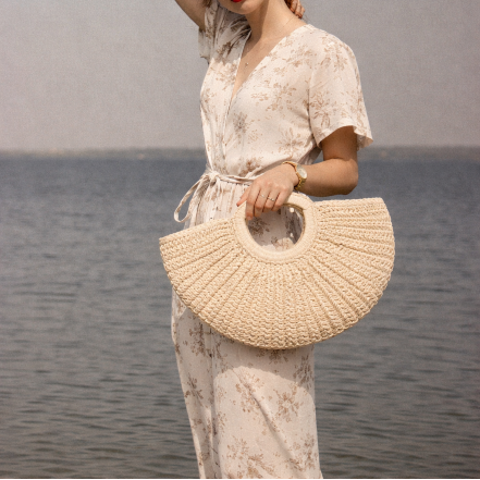 Woman holding a woven bag by the water with a neutral background