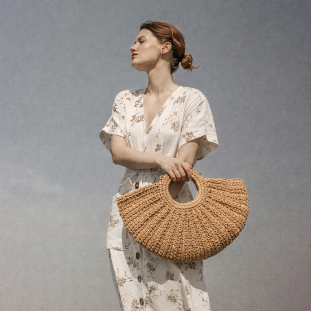Woman holding a woven handbag against a plain background
