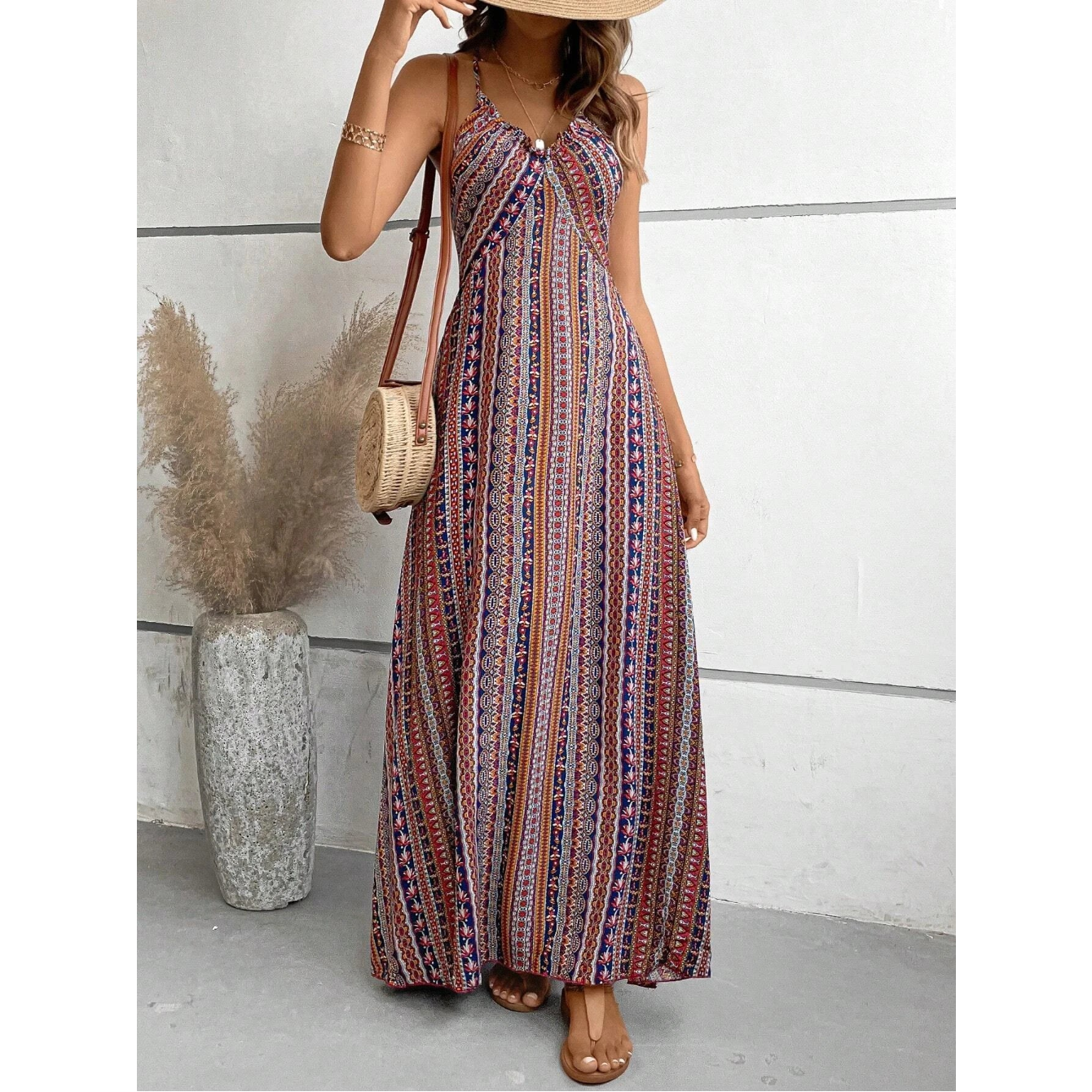 Woman wearing a patterned dress holding a straw bag against a white wall.