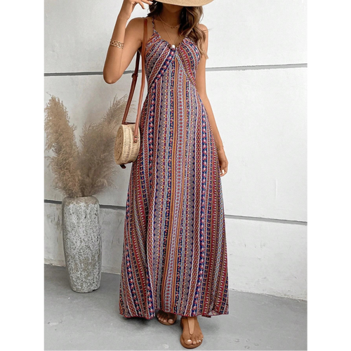 Woman wearing a patterned dress holding a straw bag against a white wall.